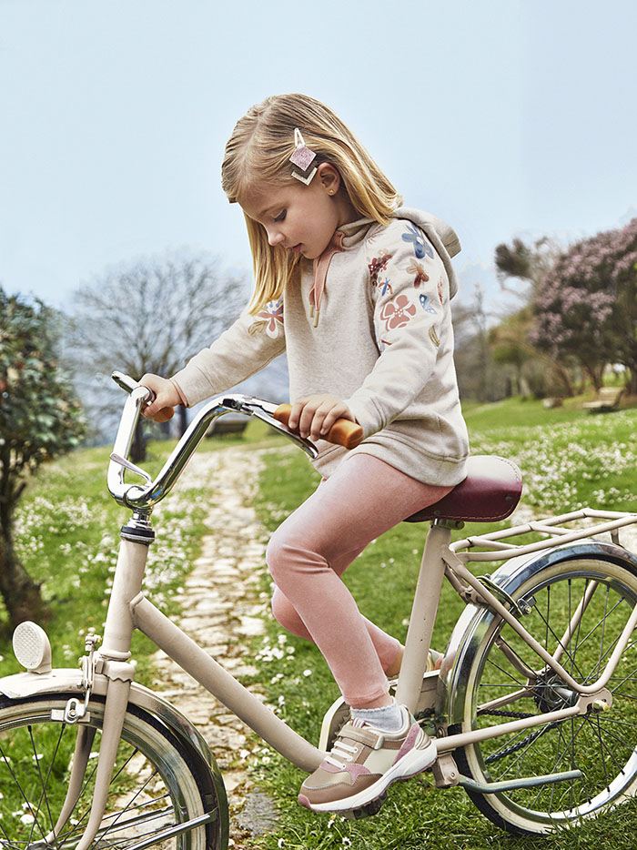 Cute little girl on a bicycle wearing pink leggings and a flower-decorated sweatshirt