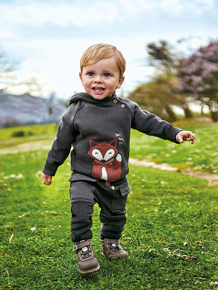 Cute toddler in a garden wearing a dark hoodie with a fox design
