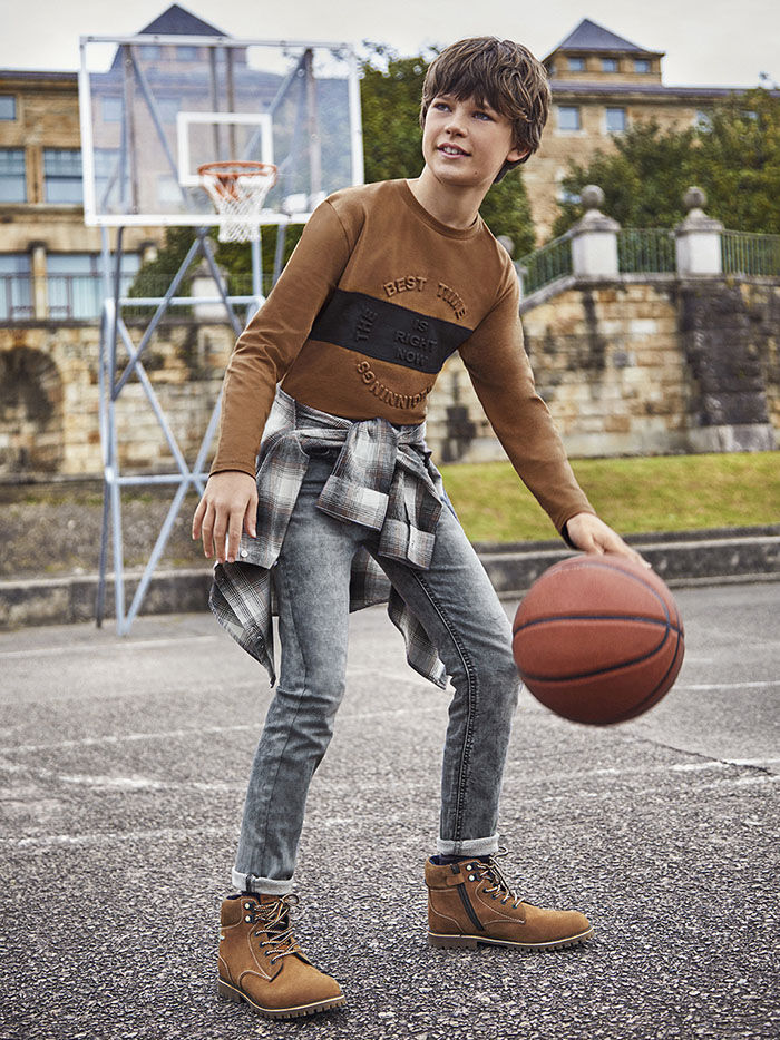 Boy on a basketball field wearing jeans, a brown sweater and leather trecking boots